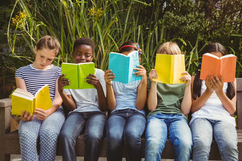 Children sitting in row and reading books at the park